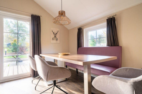 Spiseområde i Boslodge ved De Wije Werelt, Holland. Lyst rum med stort bord, sofa og vinduer med gardiner.