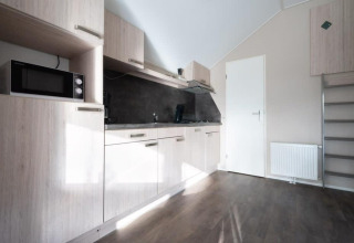 Modern kitchenette with wooden cabinets, microwave, and dark flooring at Boslodge in De Wije Werelt, Netherlands.