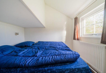 Værelse i Boslodge på De Wije Werelt, Nederlandene, med blå sengetøj og stort vindue.