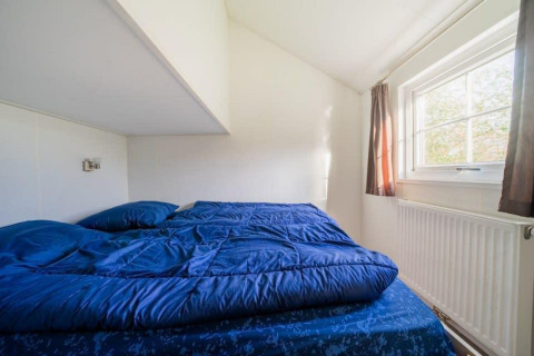 Dormitorio en Boslodge en De Wije Werelt, Países Bajos, con ropa de cama azul y ventana soleada.