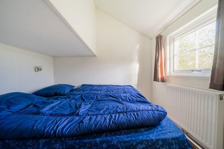 Dormitorio en Boslodge en De Wije Werelt, Países Bajos, con ropa de cama azul y ventana soleada.