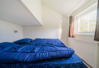 Dormitorio en Boslodge en De Wije Werelt, Países Bajos, con ropa de cama azul y ventana soleada.