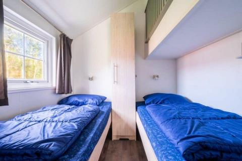 Dos camas individuales con ropa de cama azul y un armario, en Boslodge en De Wije Werelt, Países Bajos.