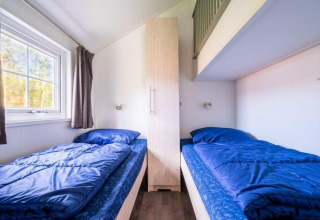 Dos camas individuales con ropa de cama azul y un armario, en Boslodge en De Wije Werelt, Países Bajos.