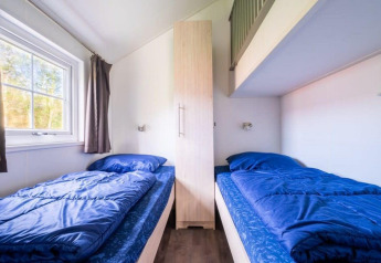 Twee eenpersoonsbedden met blauwe lakens en een kast bij Boslodge in De Wije Werelt, Nederland.