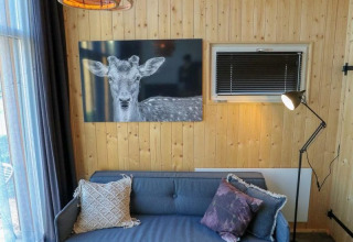 Gemütliches Wohnzimmer eines Tiny House in Buitenhuizen, Niederlande, mit Holzwänden und Hirschbild.