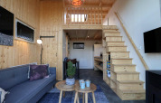 Modernes Tiny House mit Holzinterieur, Treppe zur Schlafempore, Sofa und Küche in Buitenhuizen, Niederlande.