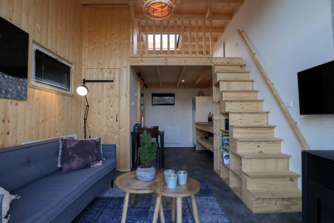 Modernes Tiny House mit Holzinterieur, Treppe zur Schlafempore, Sofa und Küche in Buitenhuizen, Niederlande.