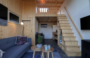 Modernes Tiny House mit Holzinterieur, Treppe zur Schlafempore, Sofa und Küche in Buitenhuizen, Niederlande.