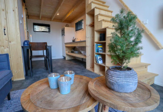 Wohnbereich im Tiny House bei Buitenhuizen, Niederlande, mit Holzmöbeln, Pflanze und Treppe.