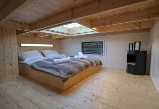 Camera da letto in legno presso Tiny House at Buitenhuizen, Olanda, con lucernario e arredamento accogliente.