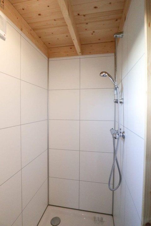 Ducha con techo de madera y azulejos blancos en el Tiny House at Buitenhuizen, Países Bajos.