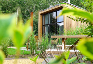 Modern tiny house bij Buitenhuizen, Nederland, omgeven door groen en met houten tuinmeubilair op het terras.