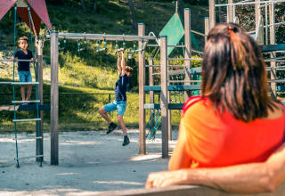 Kinderen spelen op een klimrek terwijl een vrouw toekijkt bij een glampingaccommodatie in de natuur.