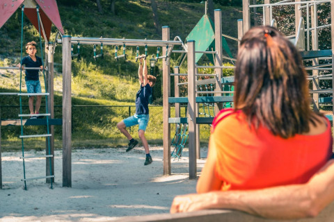 Niños jugando en una estructura de juegos bajo la mirada de una mujer en un alojamiento de glamping.