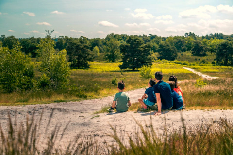 Een gezin zit samen te genieten van de natuur bij hun glamping-accommodatie, met velden en bomen.