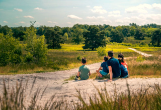 Een gezin zit samen te genieten van de natuur bij hun glamping-accommodatie, met velden en bomen.