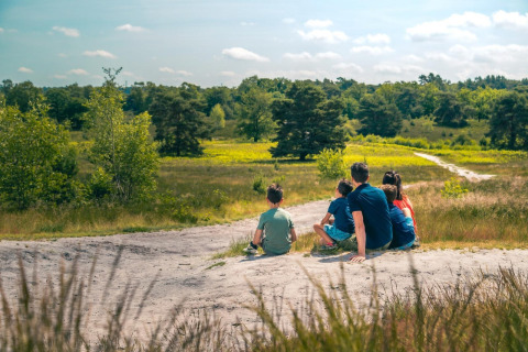 Een gezin zit samen te genieten van de natuur bij hun glampingverblijf, omgeven door groen en bomen.