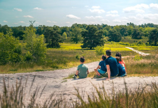 Een gezin zit samen te genieten van de natuur bij hun glampingverblijf, omgeven door groen en bomen.