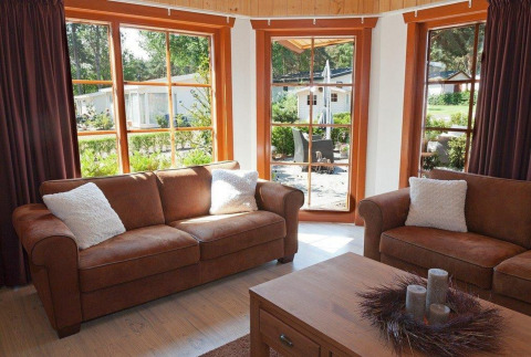 Sala de estar con sofás marrones y grandes ventanas en Boekhorst Royal + Sauna, Brunssummerheide, Países Bajos.