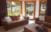 Wohnzimmer mit braunen Sofas und großen Fenstern in Boekhorst Royal + Sauna, Brunssummerheide, Niederlande.