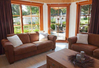 Woonkamer met bruine zetels en grote ramen in Boekhorst Royal + Sauna, Brunssummerheide, Nederland.
