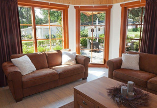 Sala de estar con sofás marrones y grandes ventanas en Boekhorst Royal + Sauna, Brunssummerheide, Países Bajos.