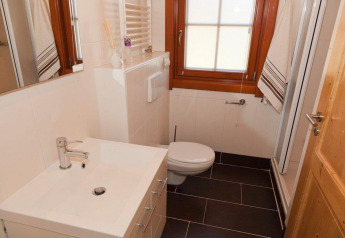 Moderne badkamer met witte lavabo, toilet, spiegel en venster in Boekhorst Royal + Sauna te Brunssummerheide, Nederland.