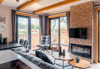 Moderne stue i tiny house Heidelodge ved Brunssummerheide, Nederlandene, med store vinduer og balkon.