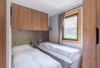 Chambre à coucher du tiny house Heidelodge, Brunssummerheide, Pays-Bas, avec deux lits simples et armoires en bois.
