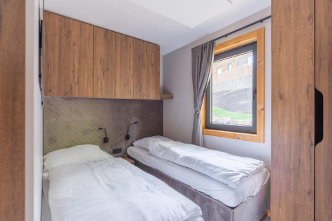 Chambre à coucher du tiny house Heidelodge, Brunssummerheide, Pays-Bas, avec deux lits simples et armoires en bois.