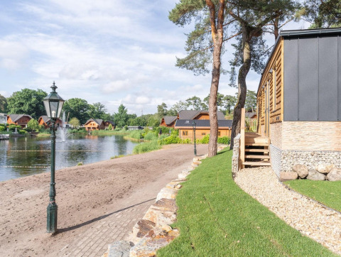 Vue du lac et des chalets en bois à Heidelodge, Brunssummerheide, Pays-Bas, entourés de verdure.
