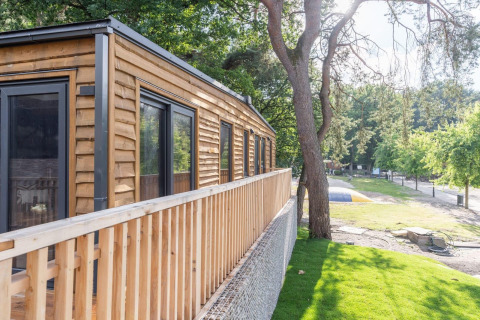 Tiny house en bois avec terrasse à Heidelodge, Brunssummerheide, Pays-Bas, entourée d’arbres et pelouse.