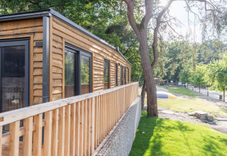 Tiny house en bois avec terrasse à Heidelodge, Brunssummerheide, Pays-Bas, entourée d’arbres et pelouse.