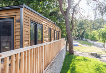 Tiny house en bois avec terrasse à Heidelodge, Brunssummerheide, Pays-Bas, entourée d’arbres et pelouse.