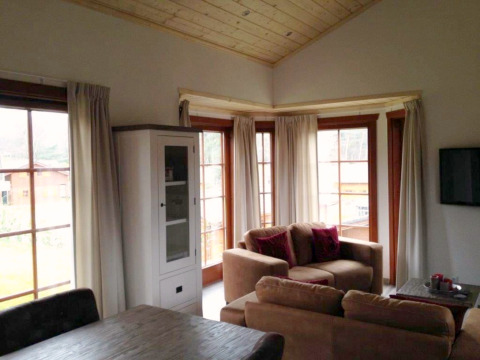Woonkamer in lodge Boekhorst bij Brunssummerheide, Nederland, met grote ramen, banken en houten plafond.