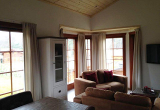 Woonkamer in lodge Boekhorst bij Brunssummerheide, Nederland, met grote ramen, banken en houten plafond.