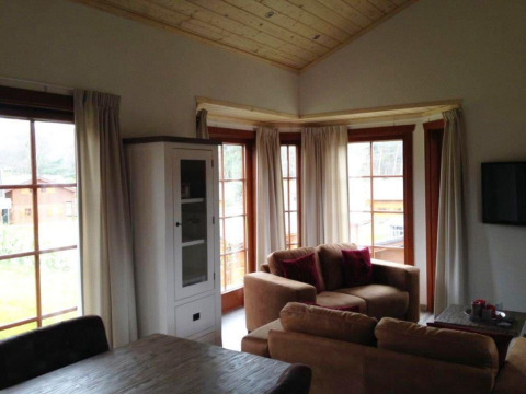 Sala de estar en la cabaña Boekhorst en Brunssummerheide, Países Bajos, con ventanales, sofás y techo de madera.