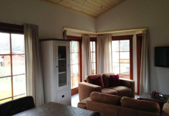 Salon du lodge Boekhorst à Brunssummerheide, Pays-Bas, avec grandes fenêtres, canapés et plafond en bois.