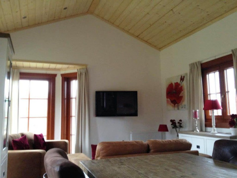 Sala de estar con techo de madera, ventanales, televisor y detalles rojos en Boekhorst Lodge en Brunssummerheide.