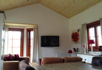 Sala de estar con techo de madera, ventanales, televisor y detalles rojos en Boekhorst Lodge en Brunssummerheide.
