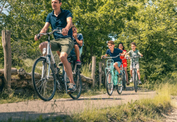 Famiglia che va in bicicletta su un sentiero immerso nel verde durante una vacanza glamping.