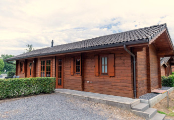 Holzlodge Boekhorst mit dunklem Ziegeldach, kleinen Fenstern und gepflegten Hecken am Rand.