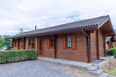 Træhytte ved Boekhorst Lodge med mørkt tag, grønne buske og grussti på en overskyet dag.
