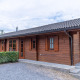Træhytte ved Boekhorst Lodge med mørkt tag, grønne buske og grussti på en overskyet dag.