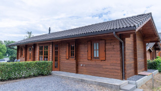Chalet en bois du Boekhorst Lodge avec toit en tuiles, haies et allée en gravier sous ciel nuageux.