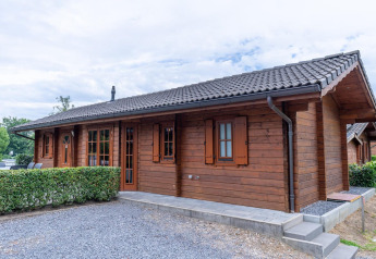 Chalet en bois du Boekhorst Lodge avec toit en tuiles, haies et allée en gravier sous ciel nuageux.