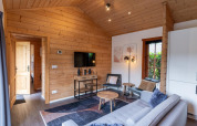 Modernes Wohnzimmer in einer Lodge mit Holzverkleidung, Sofa, Fernseher und Fenster, Boekhorst Brunssummerheide, Niederlande.