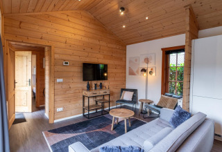 Soggiorno moderno in lodge con pareti in legno, divano, TV e finestra a Boekhorst Brunssummerheide, Paesi Bassi.