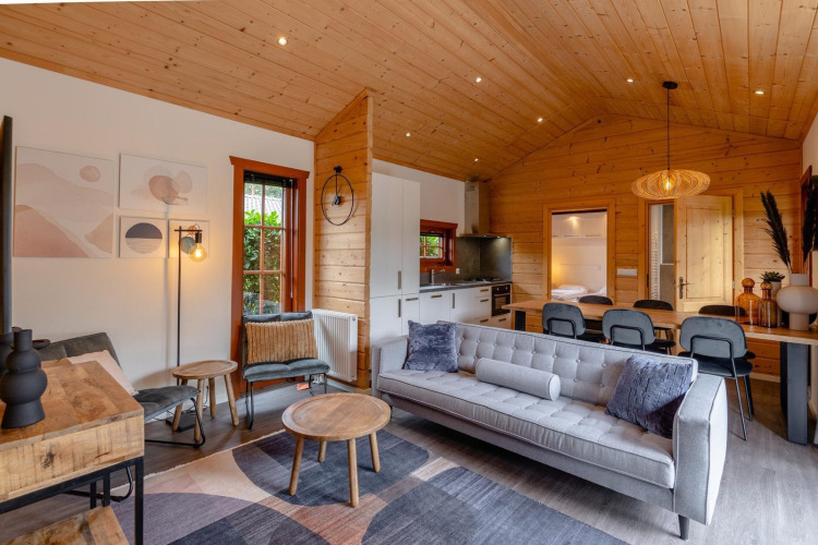 Sala de lodge moderna con techos de madera, sofá gris, mesa de comedor y cocina en Boekhorst, Brunssummerheide.